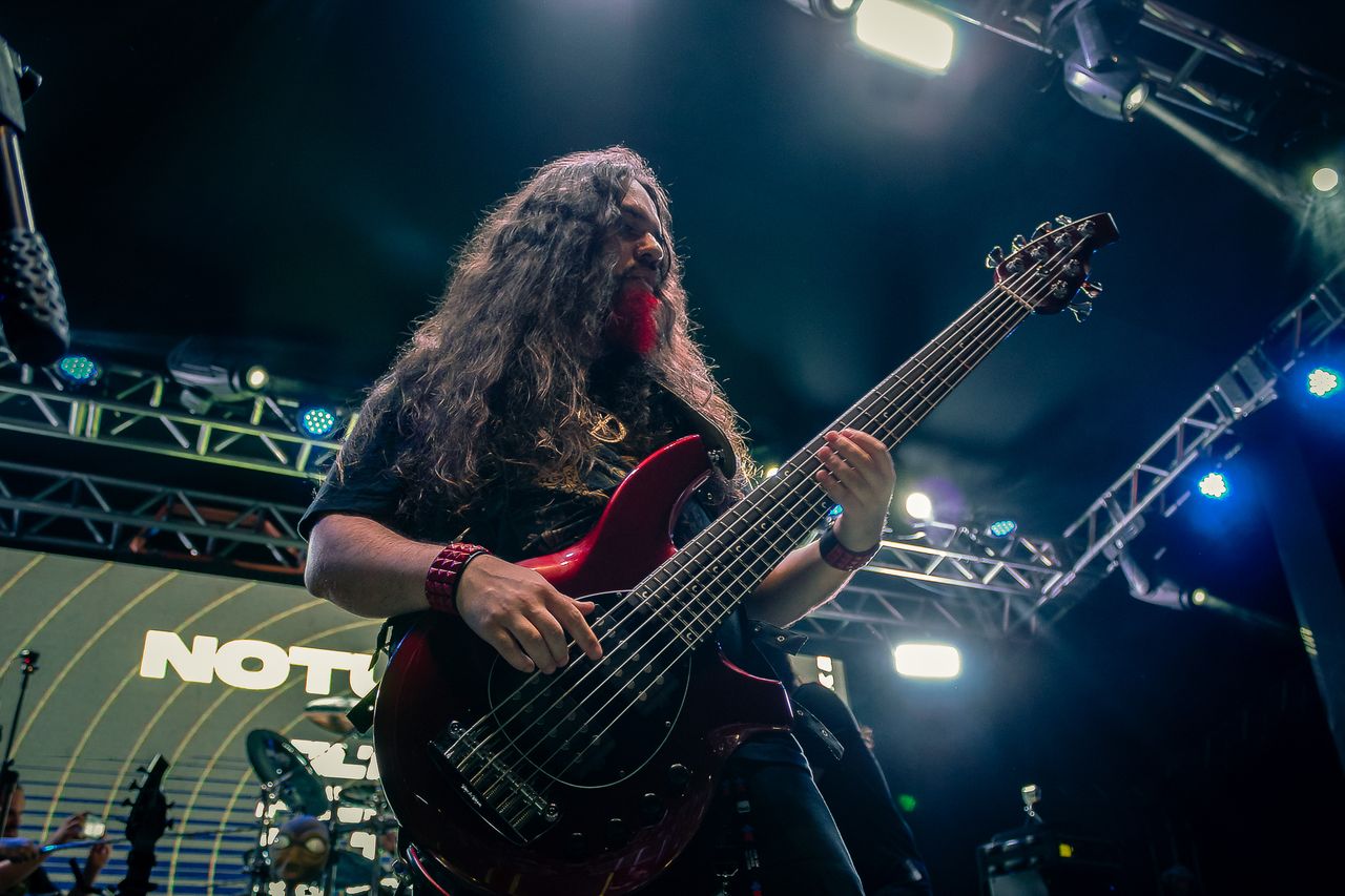 A rock musician passionately playing bass guitar on stage with vibrant lights during a concert in Brazil.